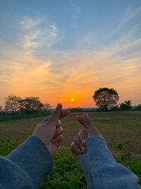Low section of people on field against sky during sunset