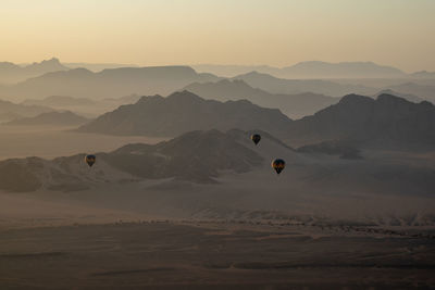 Hot air balloons flying over mountains against sky during sunrise, namib desert