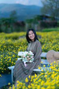 Portrait of smiling young woman with yellow flower in field