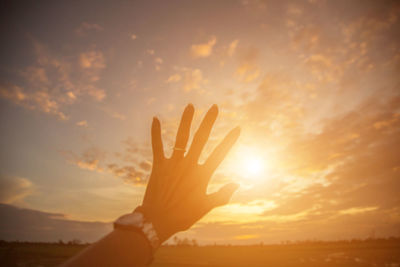 Cropped hands of woman reaching cloudy sky during sunset