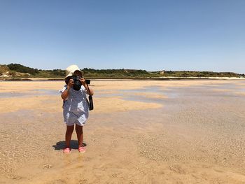 Rear view of woman standing on beach against clear sky