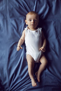 Baby boy blonde in white bodysuit lying on the bed