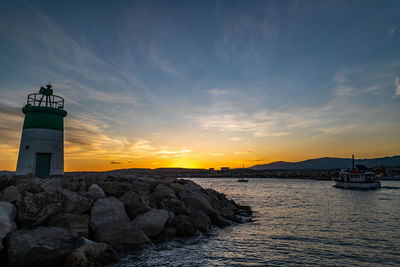 Lighthouse by sea against sky during sunset