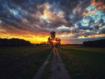 Road amidst field against sky during sunset