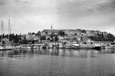 Sailboats moored in harbor by city against sky