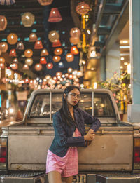 Portrait of teenage girl standing against pick-up truck at illuminated street