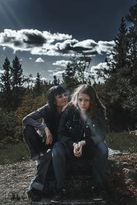 Young couple sitting on tree against sky