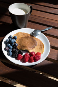 Pancakes with cranberries and grapes on a plate with a cup of milk on a table