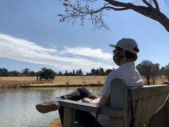 Side view of man sitting by lake against sky