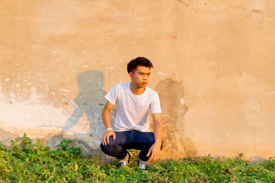 Full length of young man sitting on wall