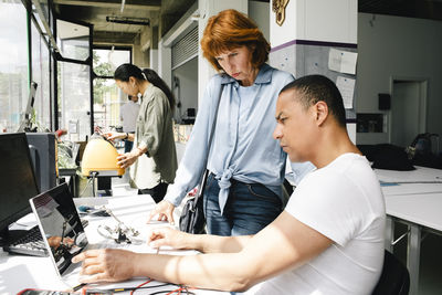 Side view of male technician examining laptop while sitting near senior woman at repair shop