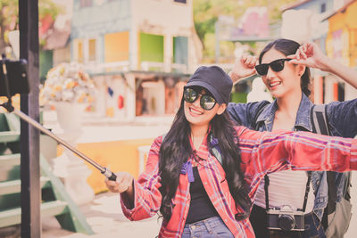 Happy friends taking selfie while standing on footpath