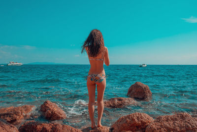 Rear view of man on rock at beach against sky