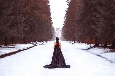 Rear view of woman standing on snow covered land amidst trees