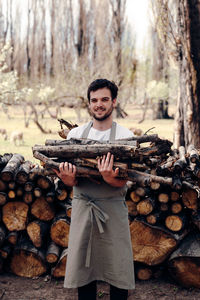 Portrait of young man standing on log in forest