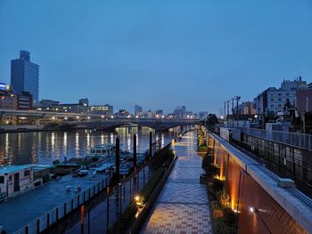 Illuminated bridge over river by buildings against sky at dusk