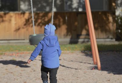 Rear view of boy running towards swing at park