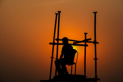 Silhouette man sitting against orange sky