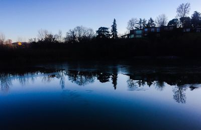 Reflection of silhouette trees in lake against sky