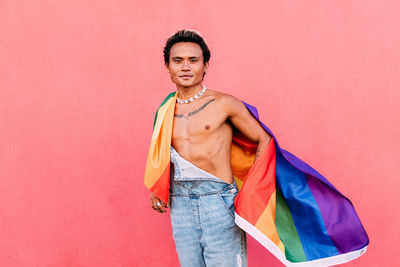 Portrait of man holding rainbow flag against pink wall