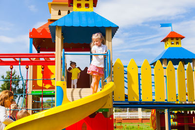 Low angle view of children on yellow playground against sky