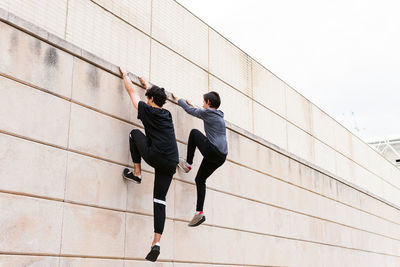 Back view of full body unrecognizable fit men in activewear taking up and jumping on wall during workout near building