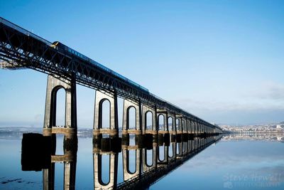 Reflection of bridge on sea against clear sky