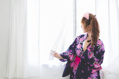 Woman looking away while standing against window at home