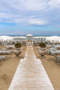 Empty table and chairs by sea against sky