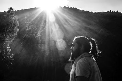 Side view of man standing in forest during sunny day