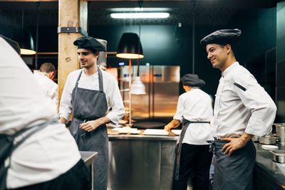 Men in hats and aprons working in team and serving dishes with delicious food in kitchen