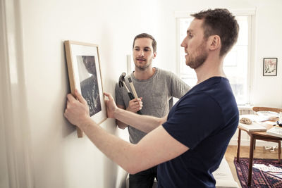 Homosexual couple hanging picture frame on wall at home