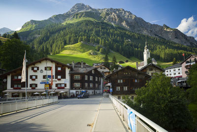 Road amidst buildings and mountains against sky