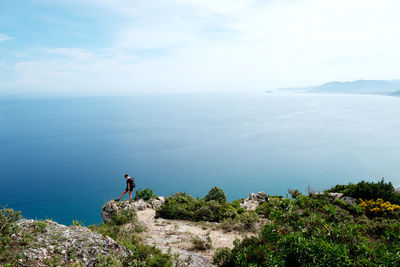 Rear view of man standing on rock by sea against sky