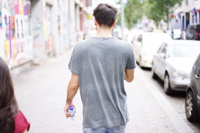 Rear view of man with water bottle walking on footpath