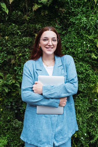 Confident businesswoman holding laptop and smiling at camera