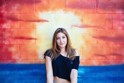 Portrait of young woman standing against brick wall