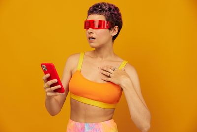 Portrait of young woman wearing sunglasses while standing against yellow background