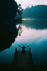 Silhouette person on pier by lake against sky