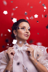 Emotional portrait of a happy brunette woman in a white dress  on a red background with confetti