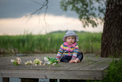 Portrait of cute baby girl sitting on pier against cloudy sky