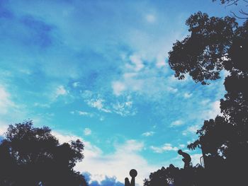 Low angle view of trees against cloudy sky