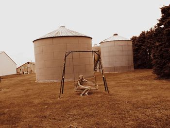 Full length of woman sitting on swing by silos at farm