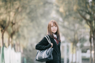 Portrait of young woman in warm clothing standing against bare trees