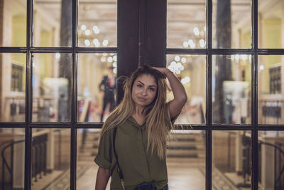 Portrait of young woman standing against window