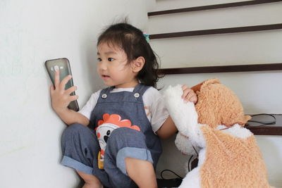 Cute baby girl playing phone cover while sitting on steps at home