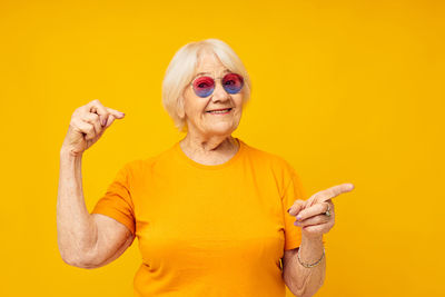 Portrait of senior woman gesturing against yellow background