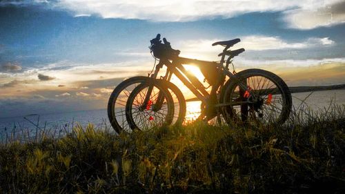 Bicycle on field by sea against sky during sunset