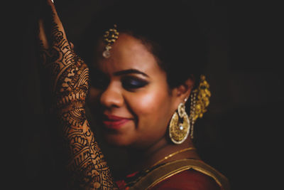 Close-up of smiling woman wearing jewelry over black background