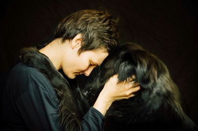 Side view of woman holding dog against black background